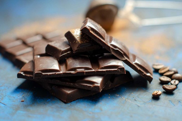 slices of dark chocolate with cocoa on a dark blue background