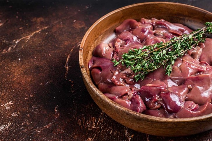 Raw chicken liver offals in a wooden plate. Dark background. Top view. Copy space