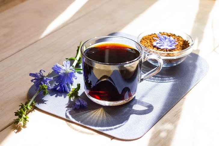 Hot natural chicory caffeine free drink in a transparent cup on a wooden table outdoors. Healthy alternative replacement for coffee, caffeine. Blue chicory flower. Beautiful summer morning at nature