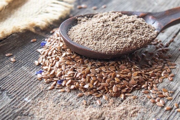 Crushed flax seed in a wooden spoon on a pile of flaxseed. Ground seed is used to prevent heart disease and being overweight.