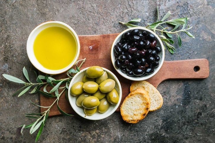 A set of Green and black olives and olive oil on a dark stone background, top view