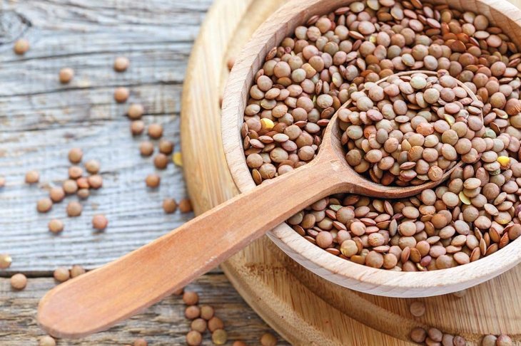 Lentils and spoon in a wooden bowl close up on an old table.