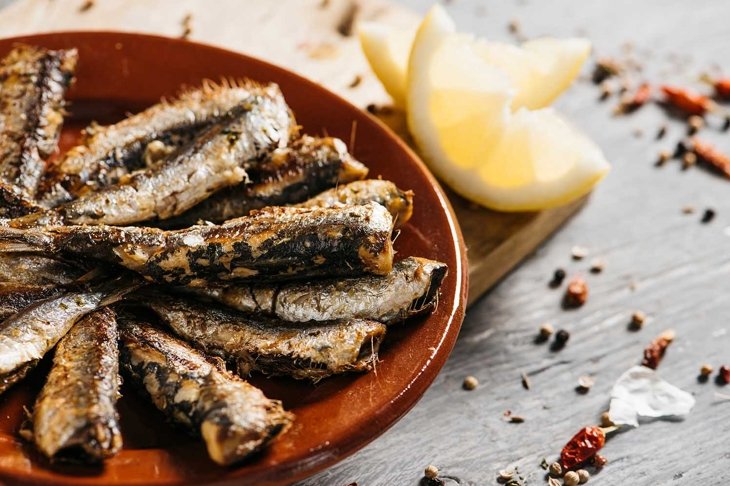 closeup of some spanish grilled sardines in a brown earthenware plate, on a gray rustic wooden table